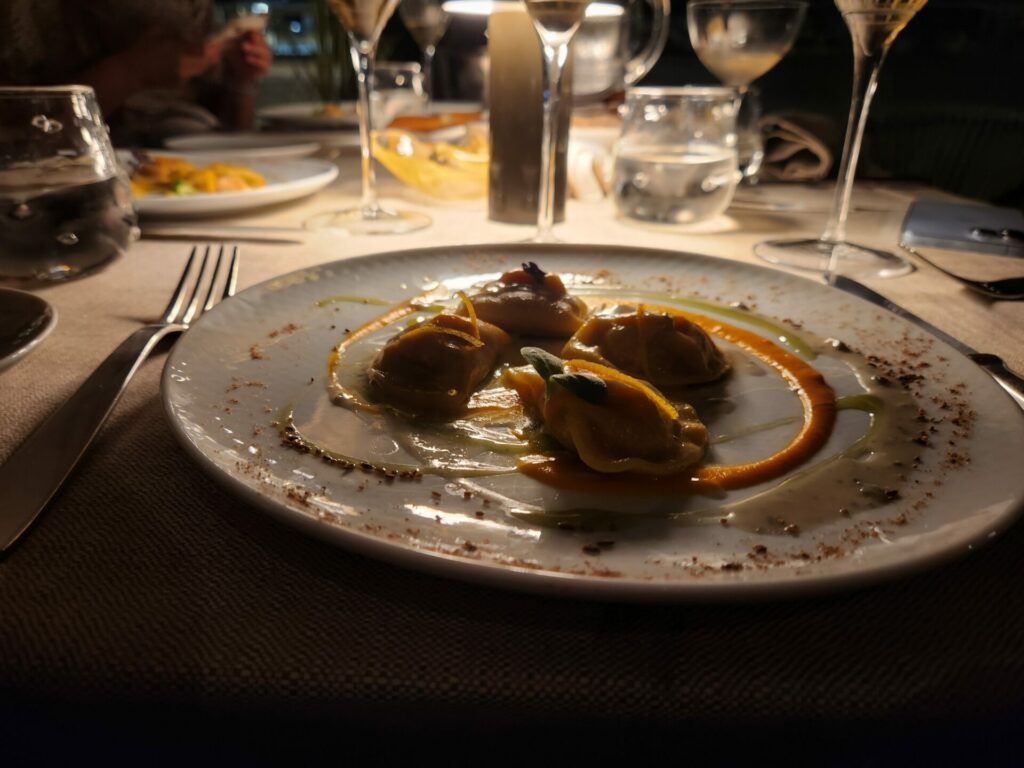 View of a plate of Italian food with wine glasses in the background