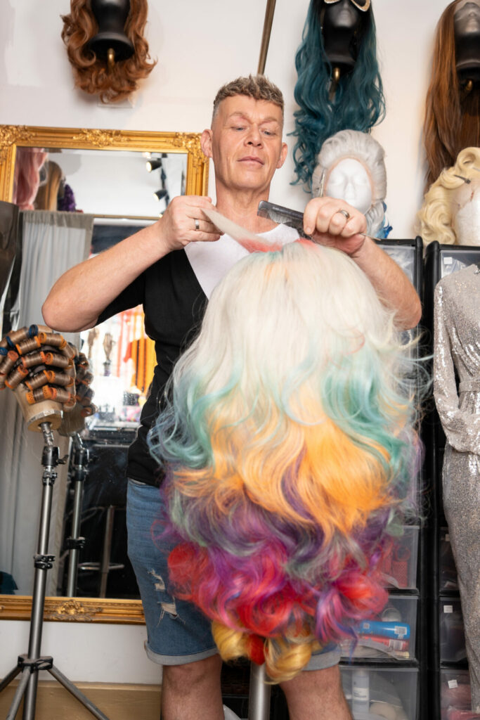 A man styles a colourful wig inside a store