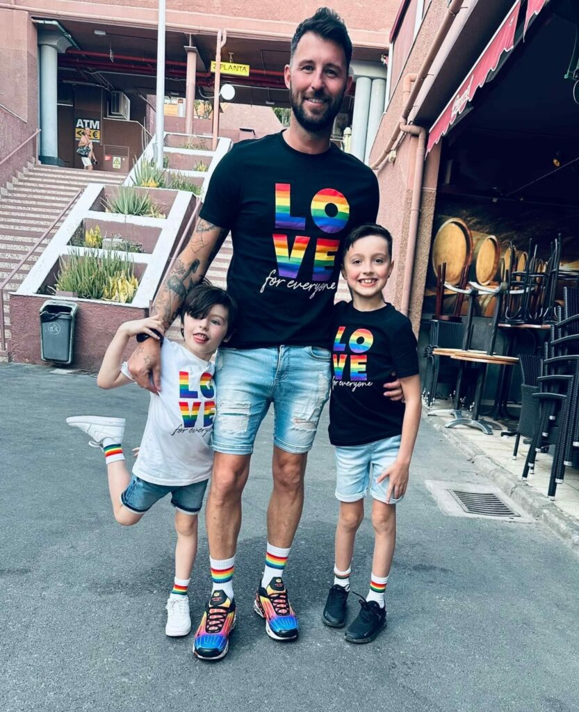 A man stands between his two young sons with his arms around them