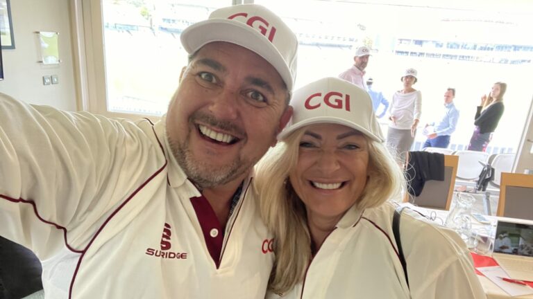 Two people wearing white CGI caps and white tops smile into the camera
