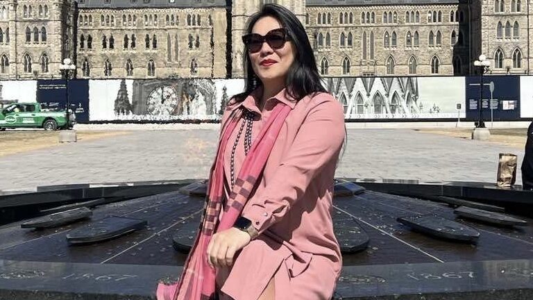 A woman wearing a pink suit sits in front of an old building