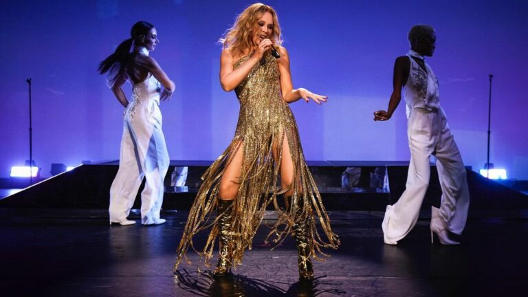 Kylie Minogue performs on stage against a blue backdrop with two dancers