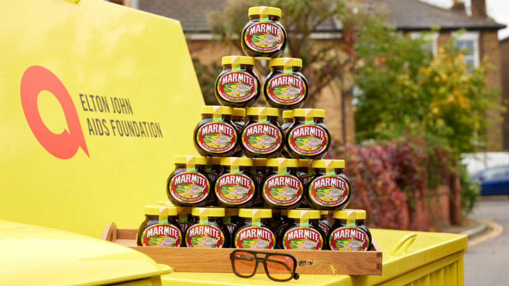 Pyramid of Marmite jars against an Elton John Aids Foundation yellow logo