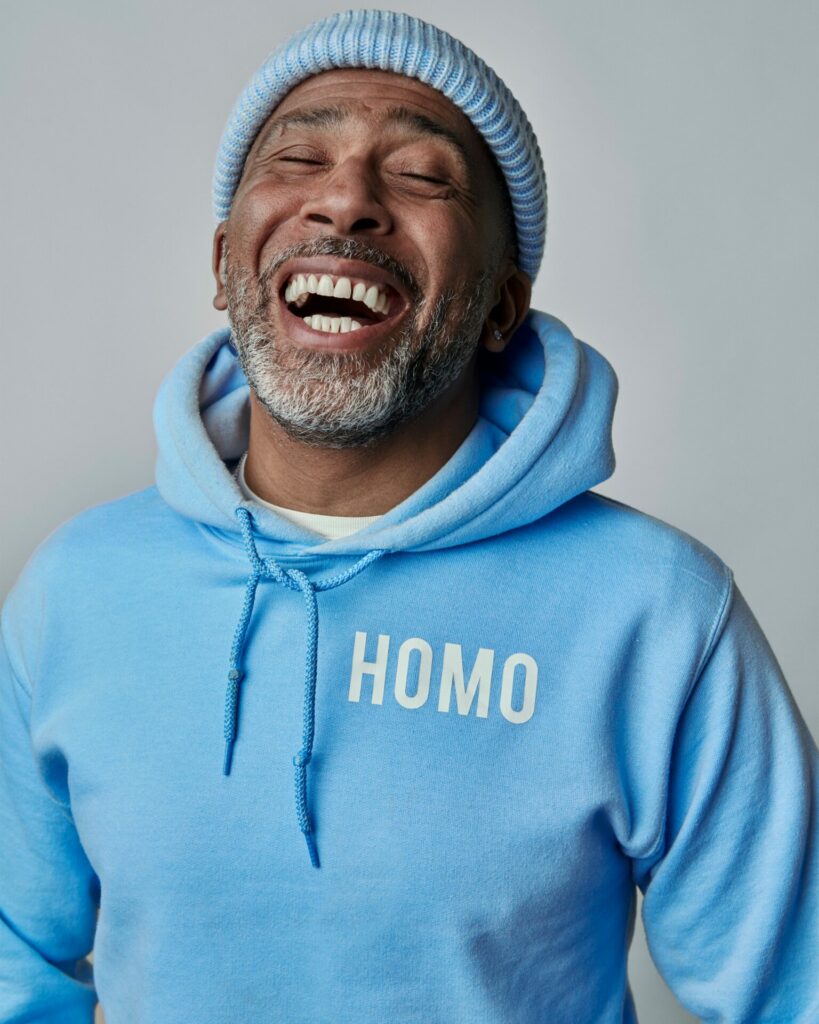 Profile shot of a laughing man wearing a blue beanie and blue hoodie with the word "homo" on it