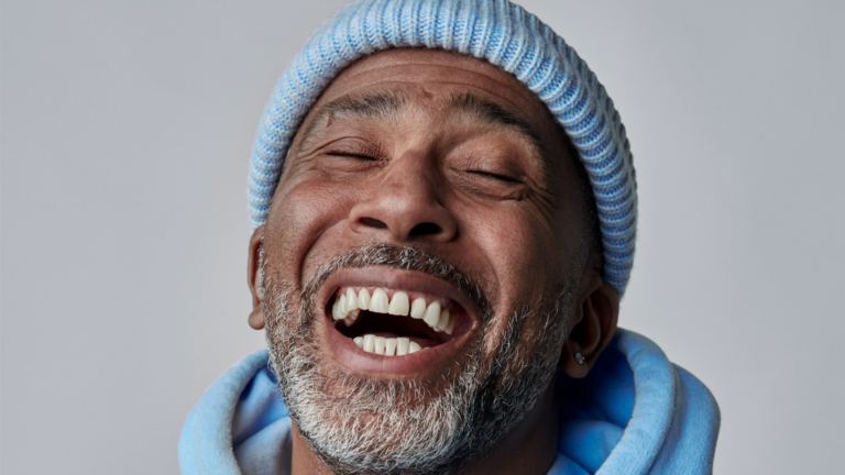 Close shot of a smiling man's face who is wearing a blue beanie hat