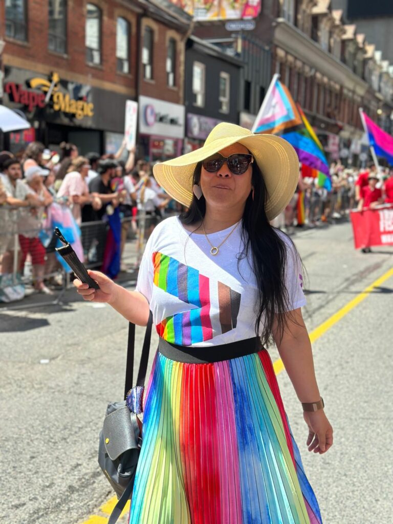 A woman wearing Pride flag clothing walks along a street during a Pride celebration