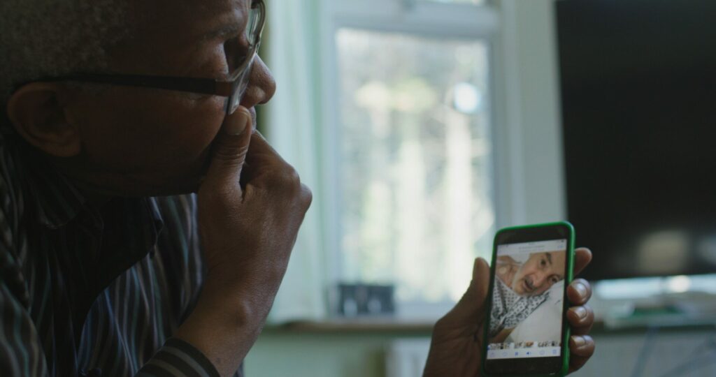 A man holds up a phone showing another man on a video on the screen