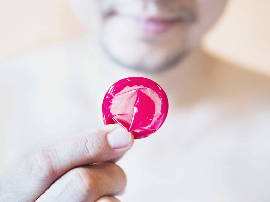 Stock image of close up a man holding a pink condom up to the camera