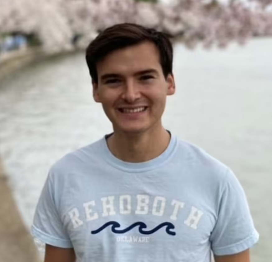 Aidan Maese-Czeropski wearing a blue T-shirt and smiling as he stands in front of a body of water