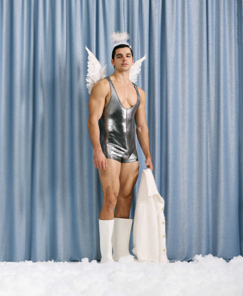 Male model wearing festive clothing poses against a silver curtain backdrop with snow at his feet