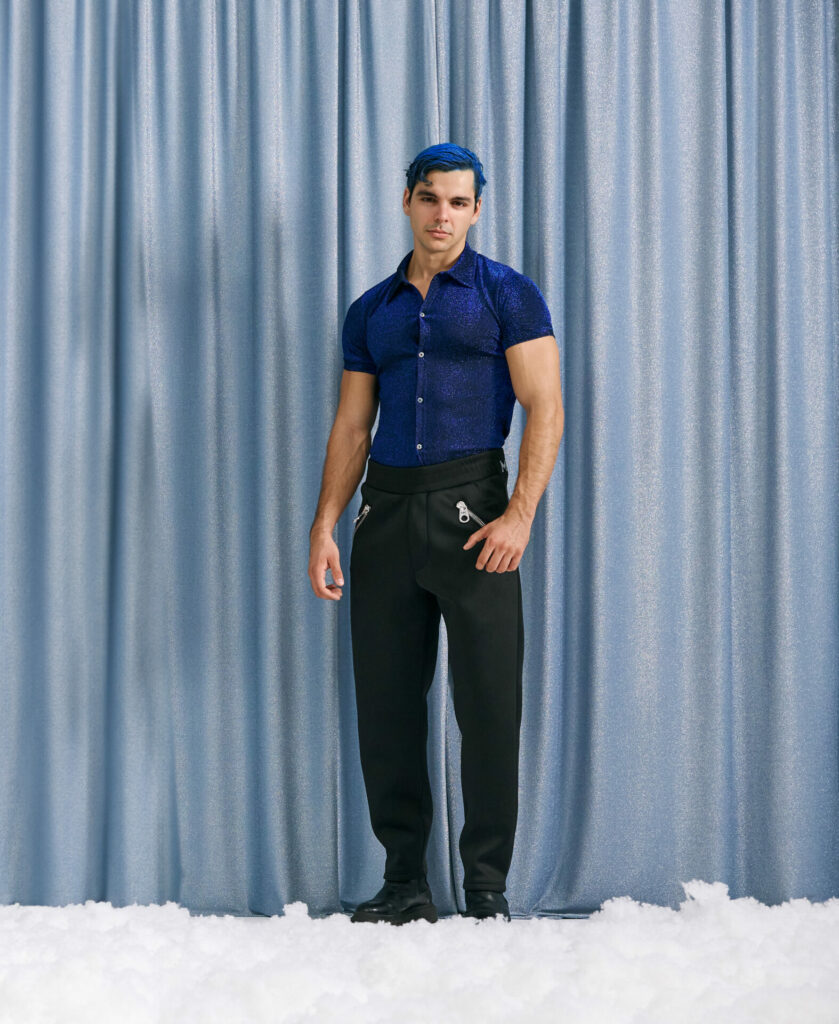 Male model wearing festive clothing poses against a silver curtain backdrop with snow at his feet