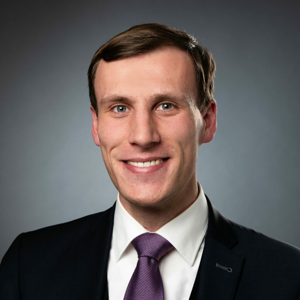 Professional headshot of a white man wearing a suit and smiling