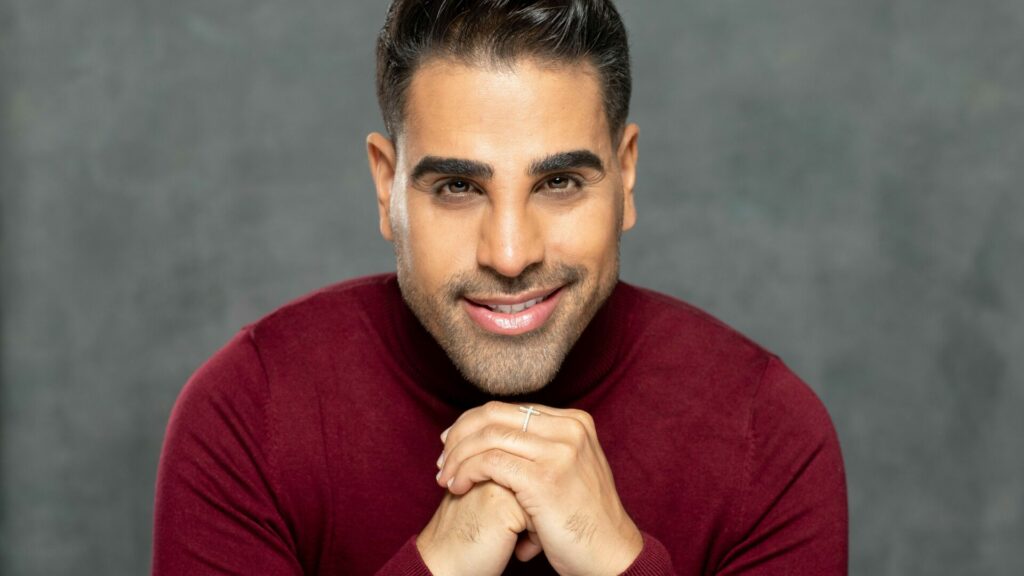 Portrait shot of Dr Ranj wearing a red jumper with his face resting on his hands