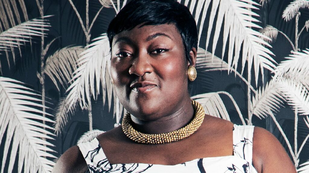 Close up of a black woman smiling against a palm leaf wallpaper backdrop