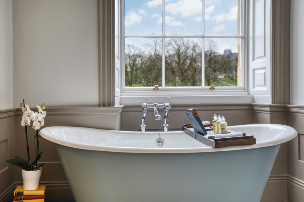 A clawfoot bath sits in a room with a sash window by it