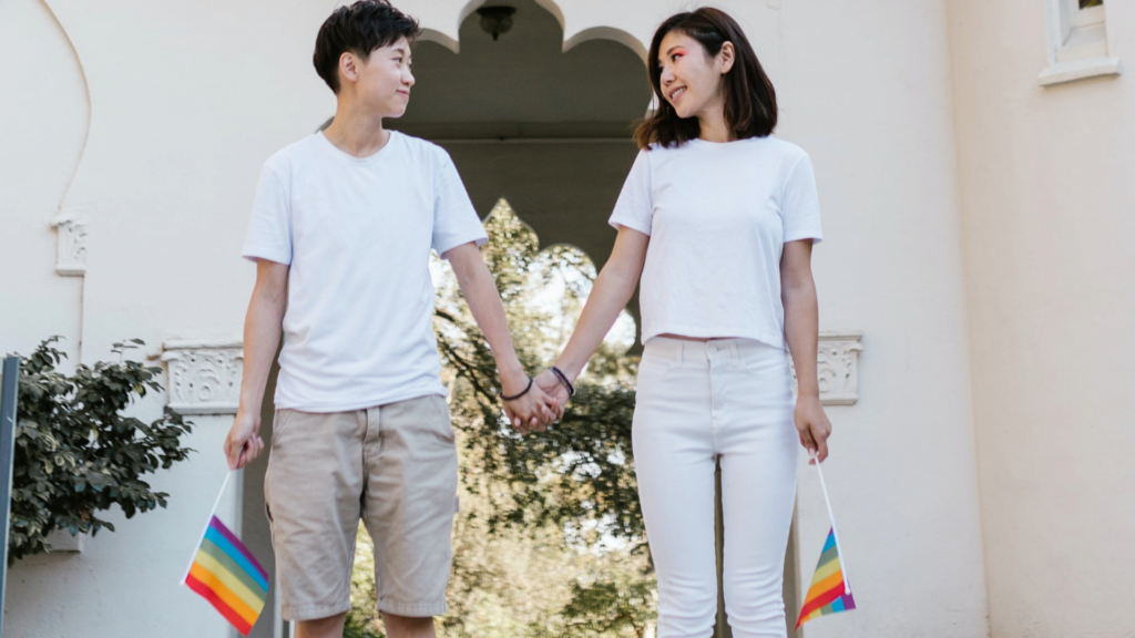Stock photo of two people holding hands and holding Pride flags