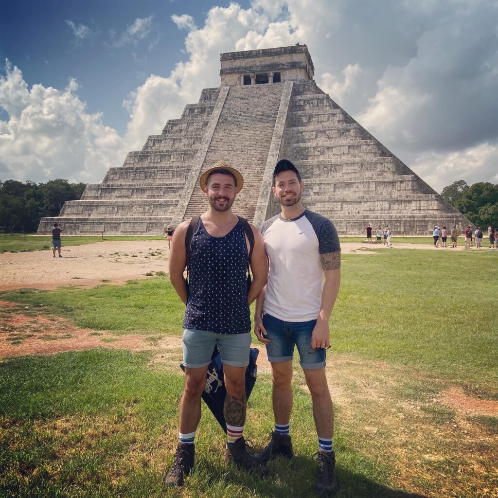 Two smiling man stand in front of the Chichén-Itzá