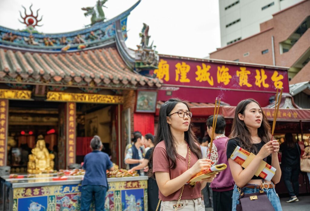 Two people hold incense outside a shrine