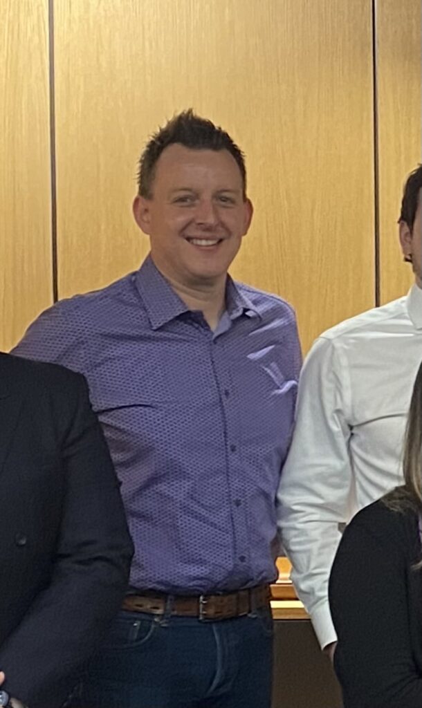 A smiling man wearing a purple shirt