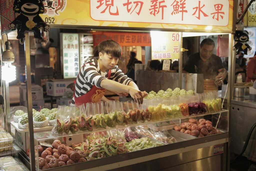 A stall worker on a food stall in a Taipei night market selling colourful fruits