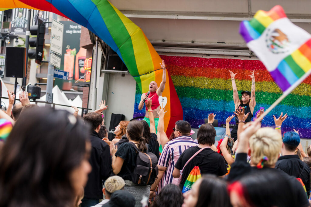 Singers perform on a stage covered in Pride flags in front of a crowd of people