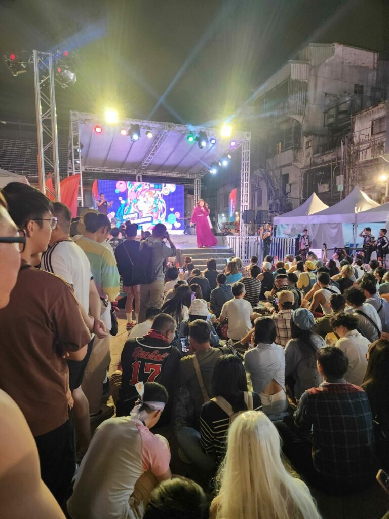 A crowd of people watch a performer onstage at night in Taipei