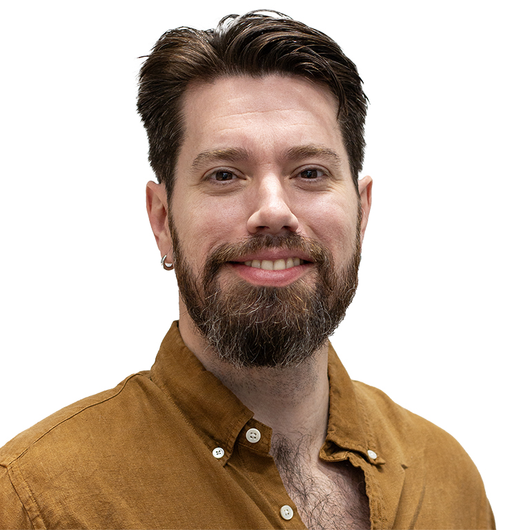 A profile shot of a smiling man with a heard wearing a tan shirt