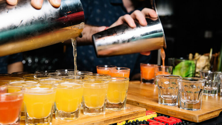 Close up of a bartender pouring a cocktail into shot glasses