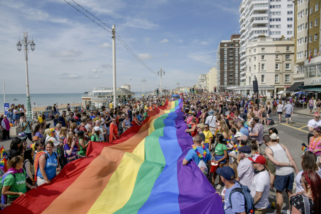 Crowds of people carry a rainbow coloured flag through Brighton
