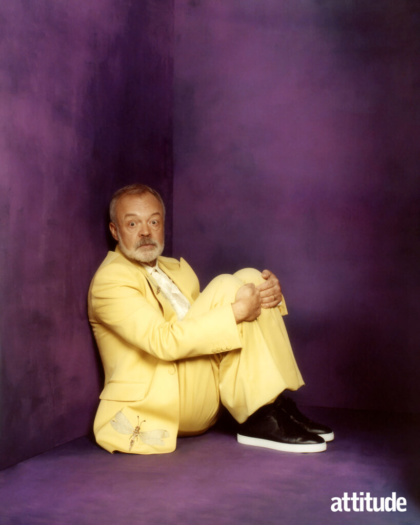 Graham sitting in a corner against a purple backdrop in a yellow suit