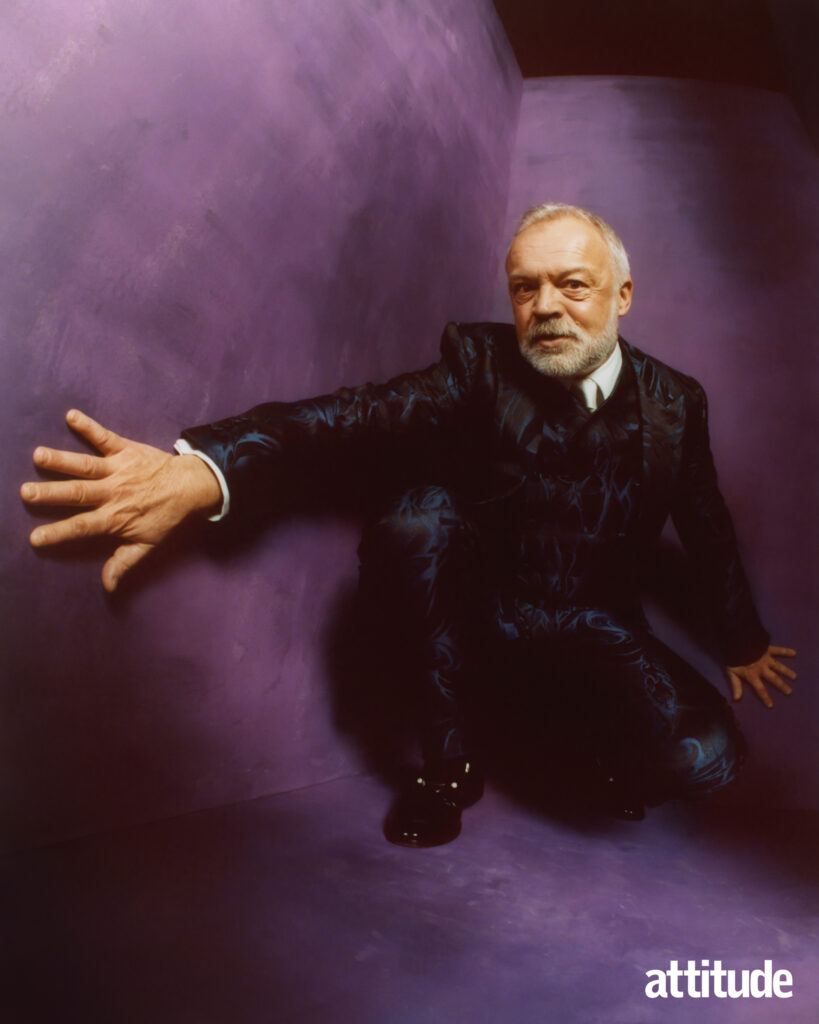 Graham Norton crouching down in a black suit against a purple backdrop