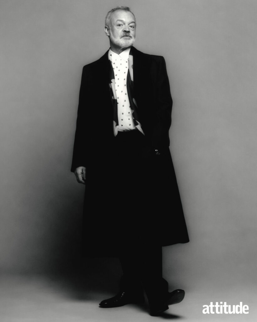 A full body shot of Graham in an overcoat, in black and white