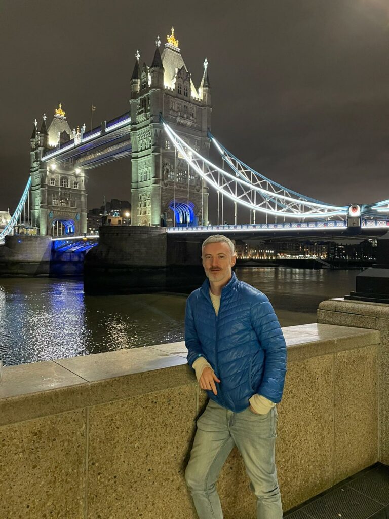 A man stands by Tower Bridge in London at night