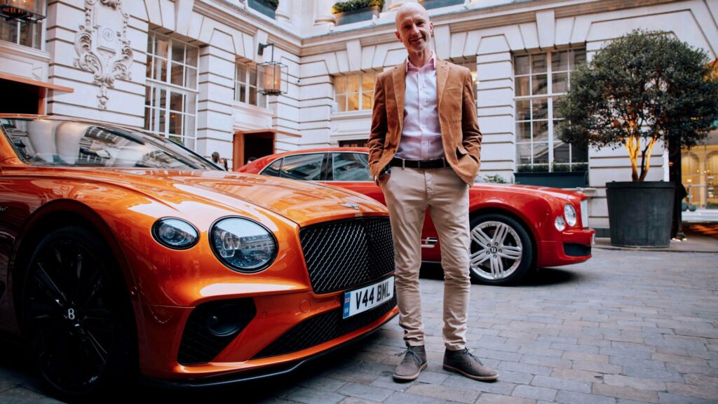 Wayne Bruce stands by two Bentley cars outside a hotel