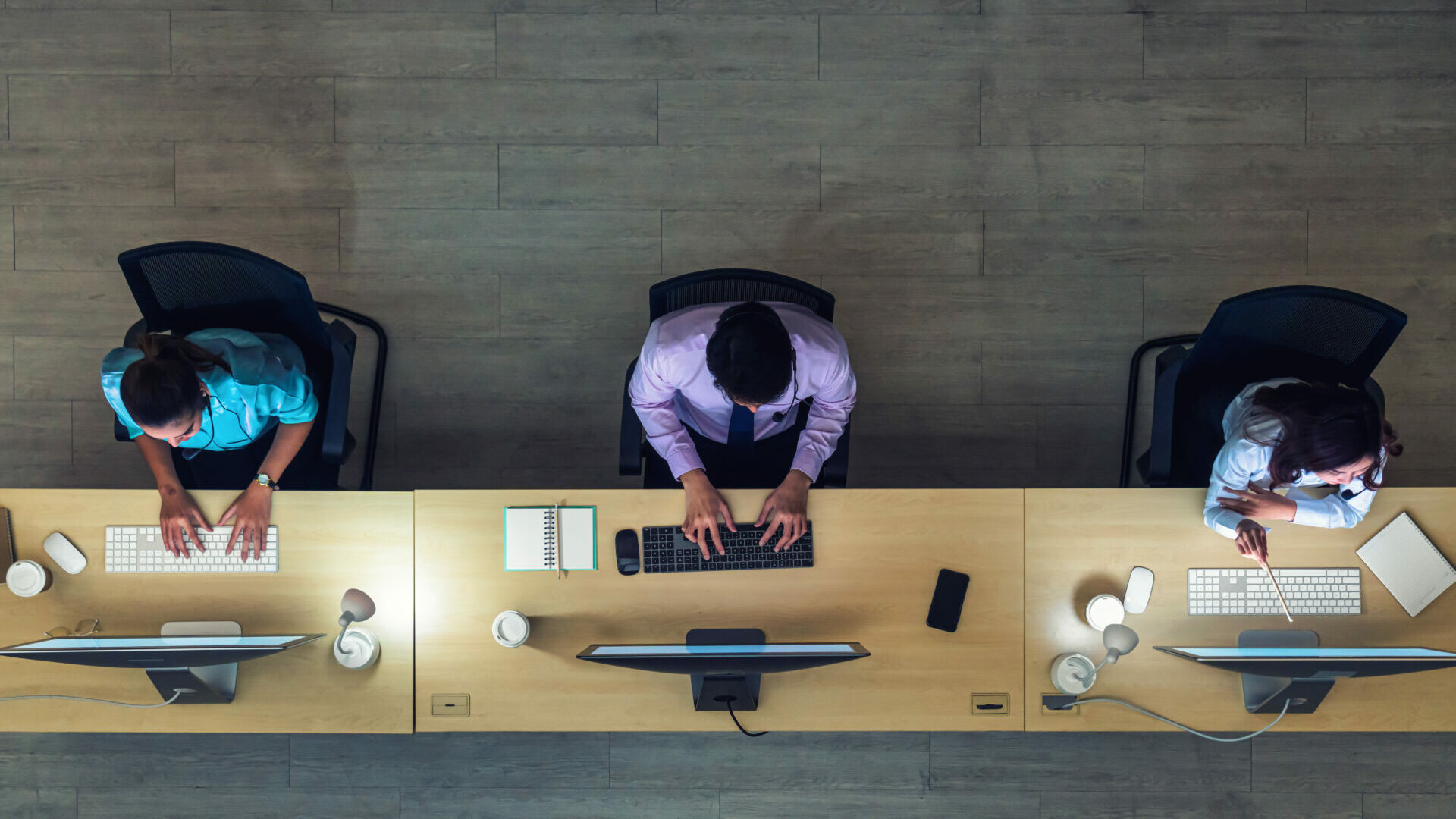 Stock photo of a top down view of 3 people working in an office sharing a long desk