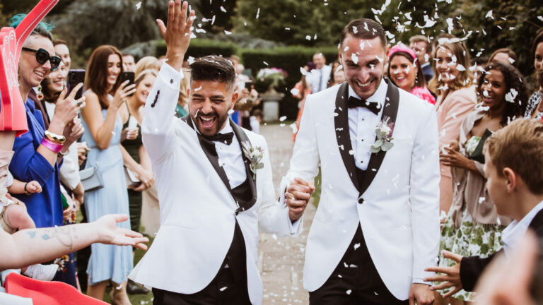 Two men on their wedding day walking among their guests and confetti