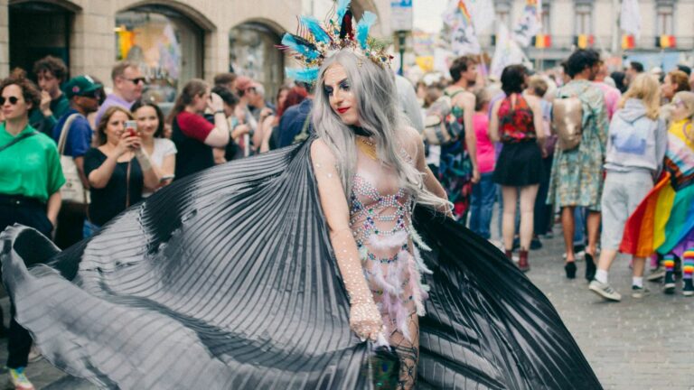 Attendees of Brussels Pride - a person wears a gray cape and twirls in the street