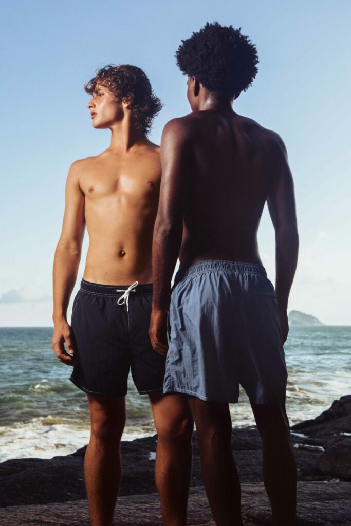 Two men pose in swimwear on a beach