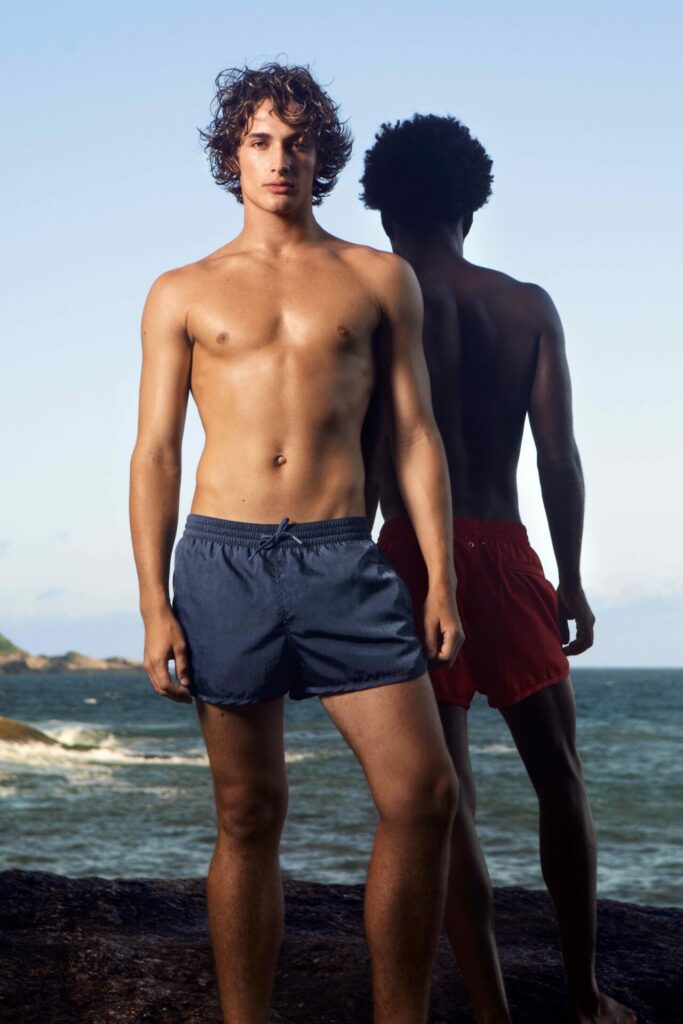 A man poses in swimwear on a beach