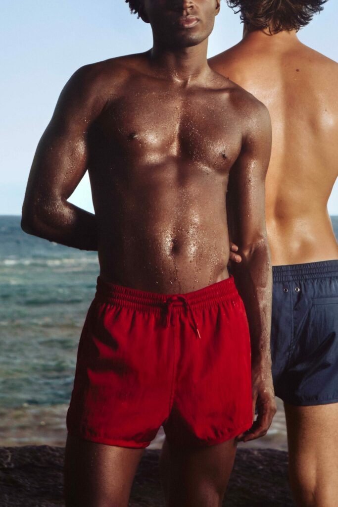 Two men pose in swimwear on a beach