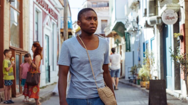 Cynthia Erivo in Drift wearing a t-shirt standing in the street in a Greek village