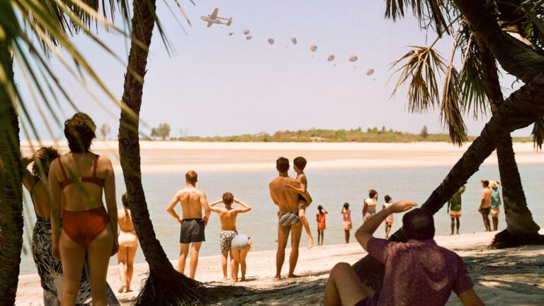 People on a beach watch a plan fly overhead