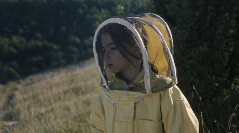 A child in a field in a beekeeper clothes