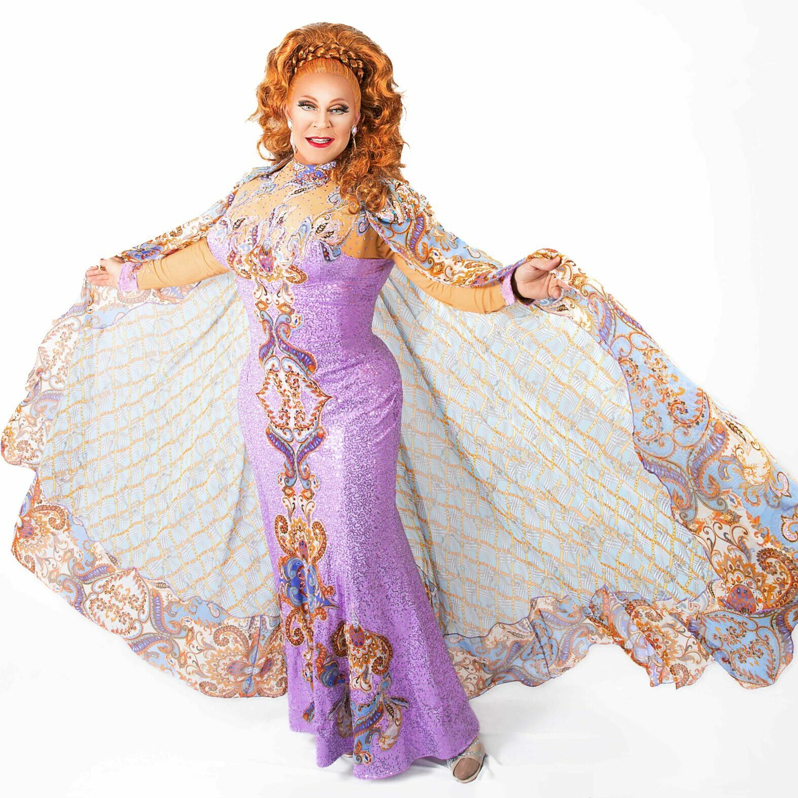 A drag queen with long red hair wearing a purple jewelled gown with a large cape