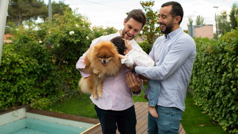 Two men hug a baby and a dog in a garden
