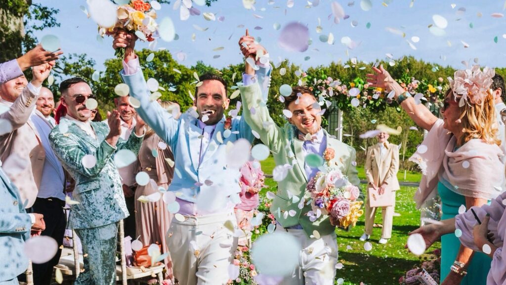 A gay couple are covered in confetti during a wedding