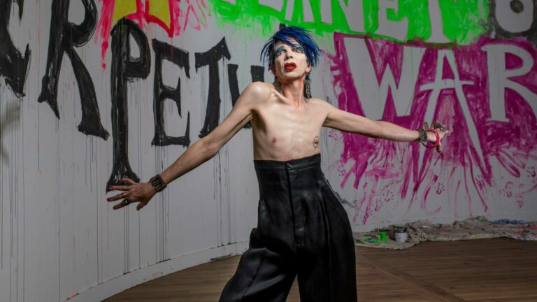 David Hoyle stands shirtless against a wall covered in graffiti