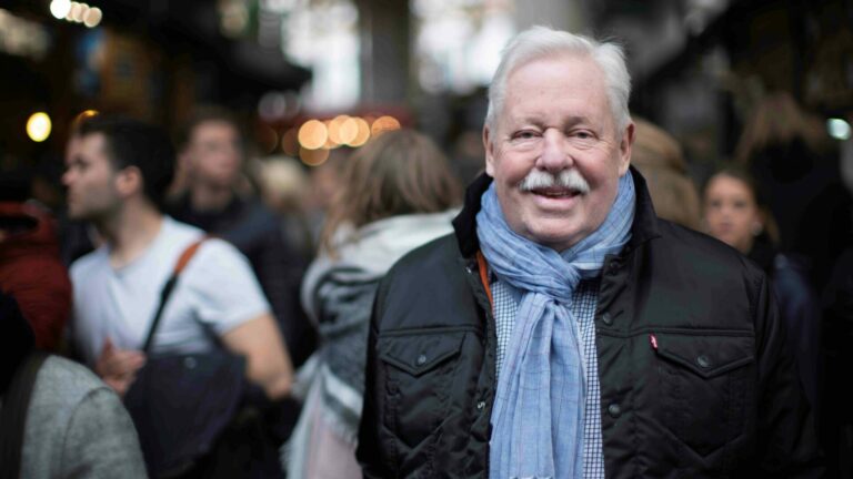 Armistead Maupin wearing a blue scarf and black gilet
