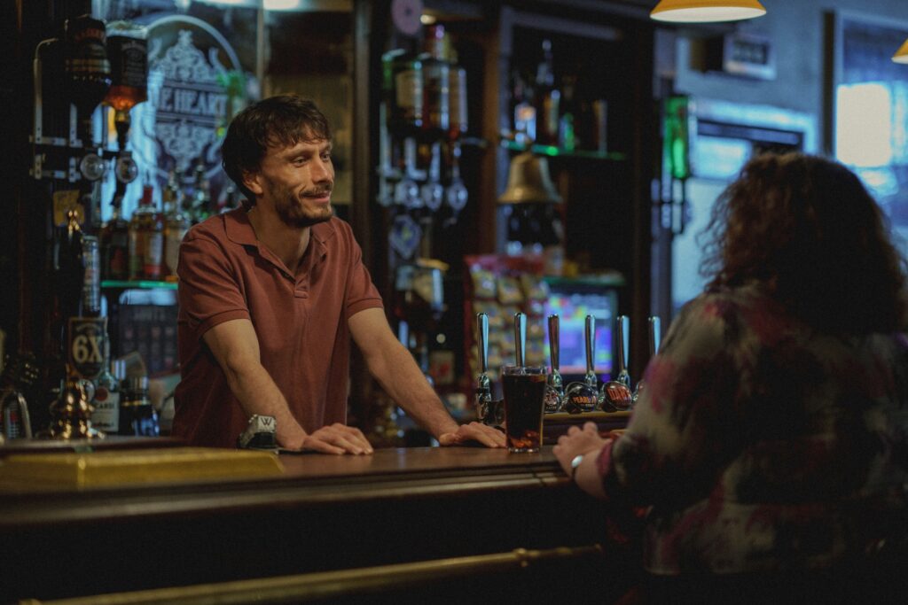 Still from Baby Reindeer showing Donny and Martha sitting at a bar chatting
