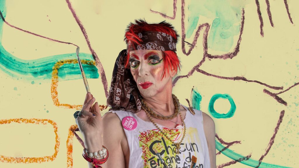 David Hoyle wearing a skull bandana and red wig holding a paintbrush